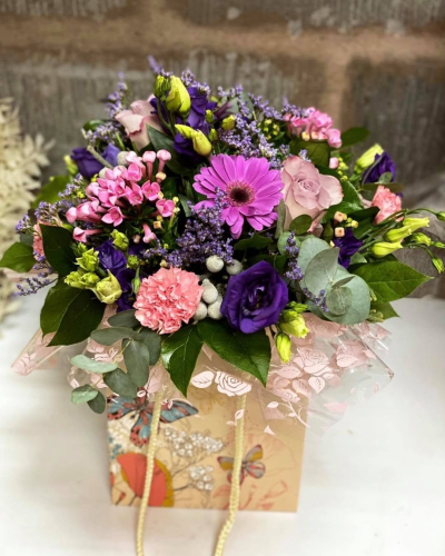 Purple Passion - A vibrant gift bag arrangement in rich purple and pink tones, finished with fresh greenery for a bold and colourful display.